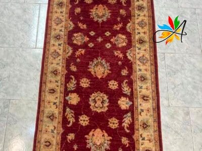 Azerbaijan Tappeti Milano Elegante tappeto tradizionale lungo con intricati motivi floreali su uno sfondo rosso intenso, disposto su un pavimento piastrellato chiaro.