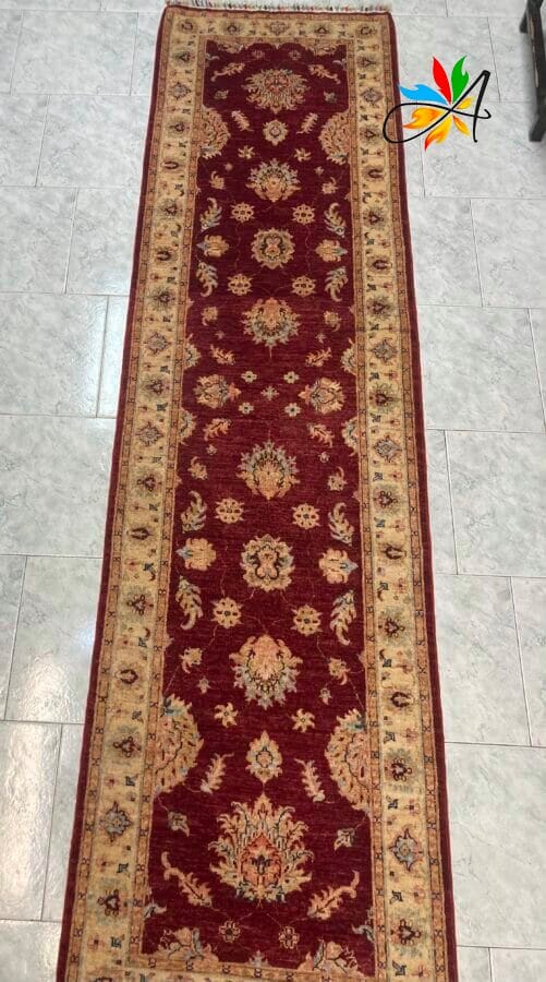 Azerbaijan Tappeti Milano Elegante tappeto tradizionale lungo con intricati motivi floreali su uno sfondo rosso intenso, disposto su un pavimento piastrellato chiaro.