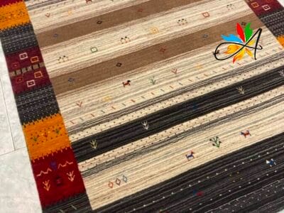 Azerbaijan Tappeti Milano Un tappeto multicolore con motivi sud-occidentali o tribali disposto su un pavimento piastrellato, caratterizzato da una decorazione a farfalla appollaiata vicino al bordo.