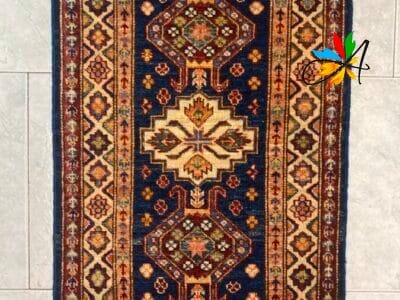 Azerbaijan Tappeti Milano Un tradizionale tappeto rettangolare con motivi intricati e un disegno a medaglione centrale esposto su un pavimento piastrellato.