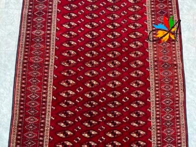Azerbaijan Tappeti Milano Un tappeto a motivi rossi con una farfalla artificiale decorativa su un angolo.