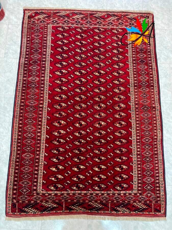 Azerbaijan Tappeti Milano Un tappeto a motivi rossi con una farfalla artificiale decorativa su un angolo.