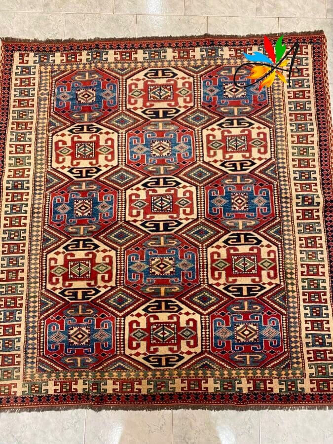 Azerbaijan Tappeti Milano Tappeto rettangolare con disegni geometrici rossi, blu e crema su un pavimento piastrellato.