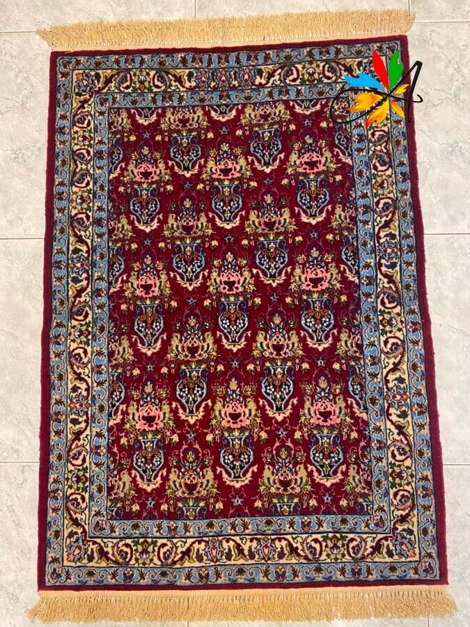 Azerbaijan Tappeti Milano Tappeto rettangolare in stile persiano con intricati motivi floreali su uno sfondo rosso intenso, un bordo decorativo blu e oro e frange gialle su entrambe le estremità corte. Nell'angolo in alto a destra compare un logo multicolore.