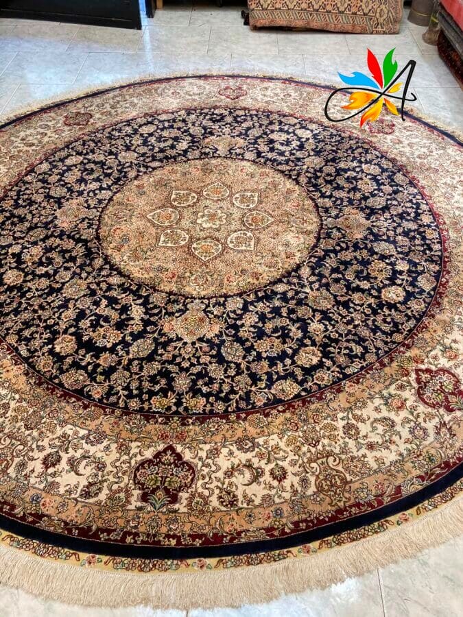 Azerbaijan Tappeti Milano Tappeto rotondo in stile persiano con intricati motivi floreali nei toni del blu, beige e rosso. Un logo colorato è posizionato in un angolo.