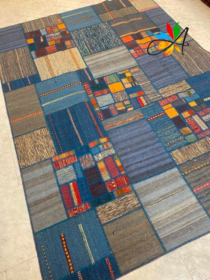 Azerbaijan Tappeti Milano Un tappeto rettangolare con un motivo patchwork composto da vari motivi e texture colorati, prevalentemente nelle tonalità del blu, disposto su un pavimento piastrellato.