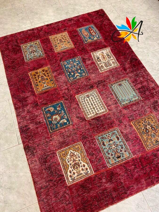 Azerbaijan Tappeti Milano Un tappeto rosso con motivo patchwork caratterizzato da vari motivi rettangolari colorati e un logo astratto in un angolo.