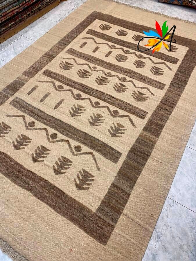 Azerbaijan Tappeti Milano Un tappeto beige e marrone intrecciato con motivi geometrici e di foglie, adagiato su un pavimento piastrellato.