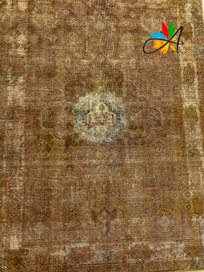 Azerbaijan Tappeti Milano Un tappeto vintage rovinato con un design a medaglione sbiadito al centro. Un logo colorato con un motivo a foglia è visibile nell'angolo in alto a destra.