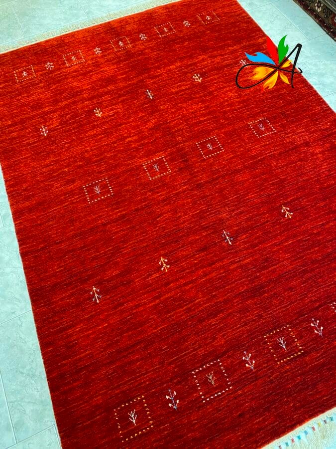 Azerbaijan Tappeti Milano Tappeto rosso con semplici motivi geometrici e floreali. Piastrelle azzurre sono visibili ai bordi. Un motivo colorato di foglie e nastri è nell'angolo in alto a destra.