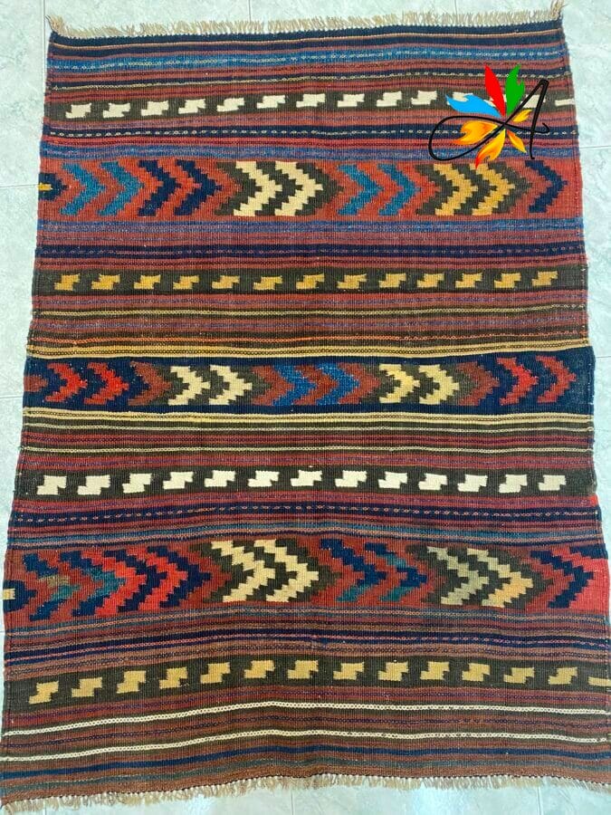 Azerbaijan Tappeti Milano Tessuto intrecciato con motivi geometrici in rosso, blu, verde, giallo e beige. In alto a destra è presente un emblema colorato.