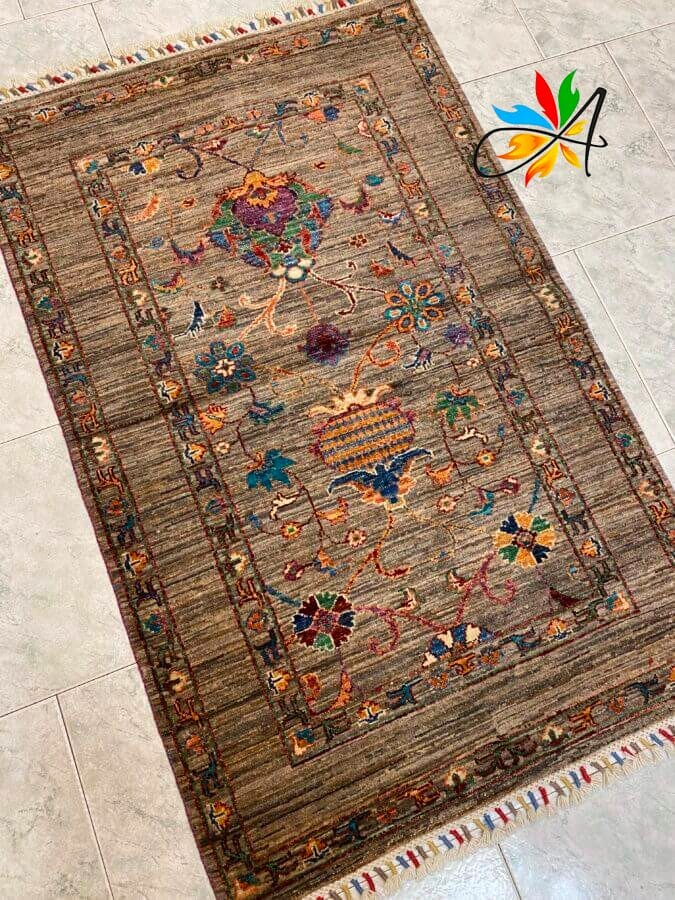 Azerbaijan Tappeti Milano Tappeto rettangolare con un tradizionale motivo floreale e geometrico, caratterizzato da un mix di toni rossi, blu e gialli su uno sfondo marrone. Bordi con frange multicolori e un emblema decorativo nell'angolo.