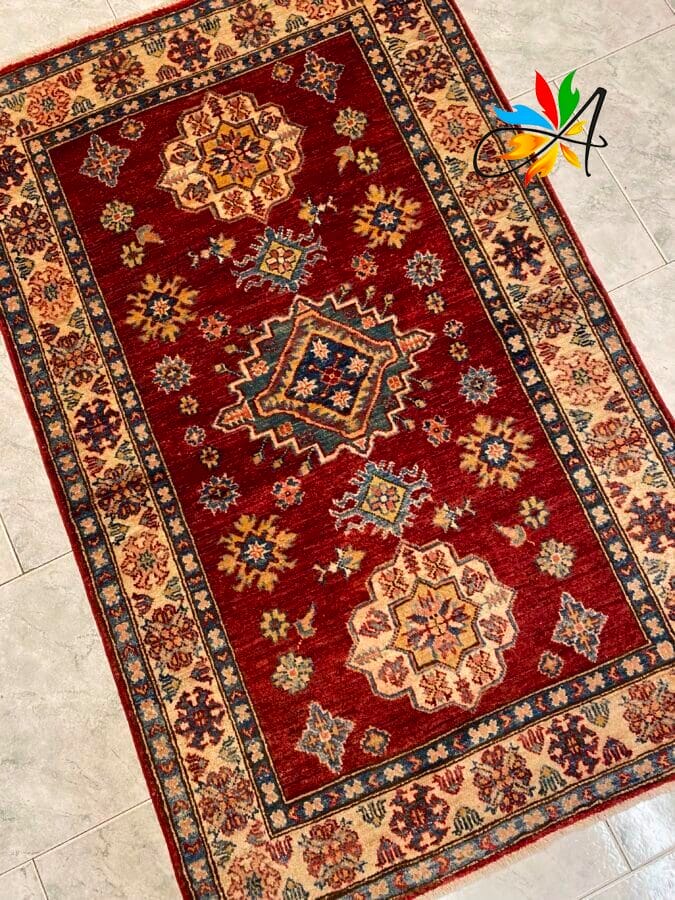 Azerbaijan Tappeti Milano Tappeto rosso con intricati disegni geometrici e floreali su pavimento piastrellato.