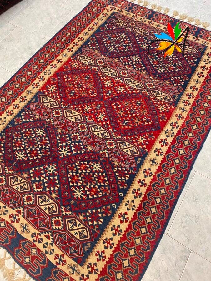 Azerbaijan Tappeti Milano Un tappeto vivace con motivi geometrici nei tradizionali colori rosso, blu e beige su un pavimento piastrellato.