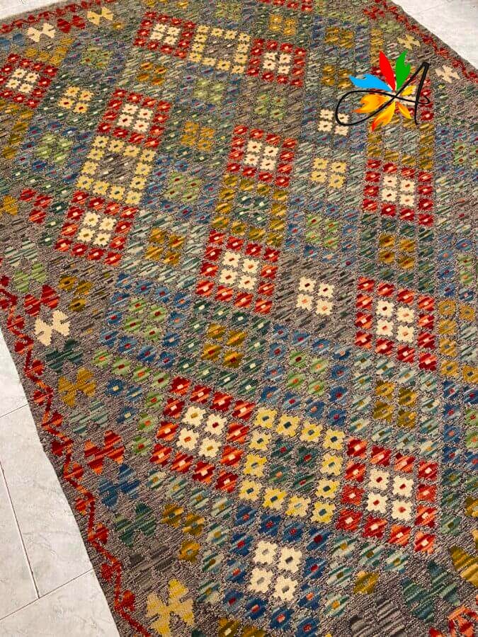 Azerbaijan Tappeti Milano Un tappeto colorato intrecciato con motivi geometrici in rosso, giallo, blu e verde, caratterizzato da un bordo con un motivo di foglie multicolori in un angolo.