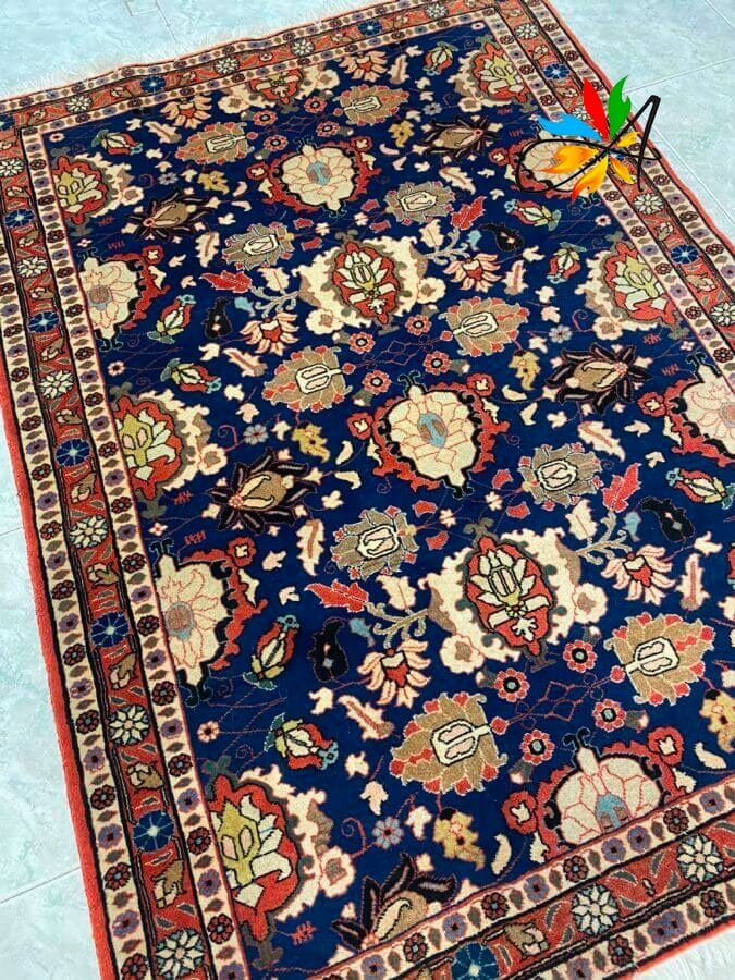 Azerbaijan Tappeti Milano Un tappeto rettangolare in stile persiano con sfondo blu scuro e intricati motivi floreali in rosso, crema e verde, bordati da motivi geometrici.