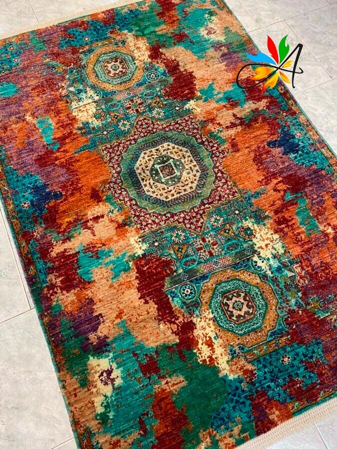 Azerbaijan Tappeti Milano Tappeto colorato con motivi geometrici a medaglioni al centro, caratterizzato da tonalità di verde acqua, arancione, rosso e crema, posizionato su un pavimento piastrellato chiaro.