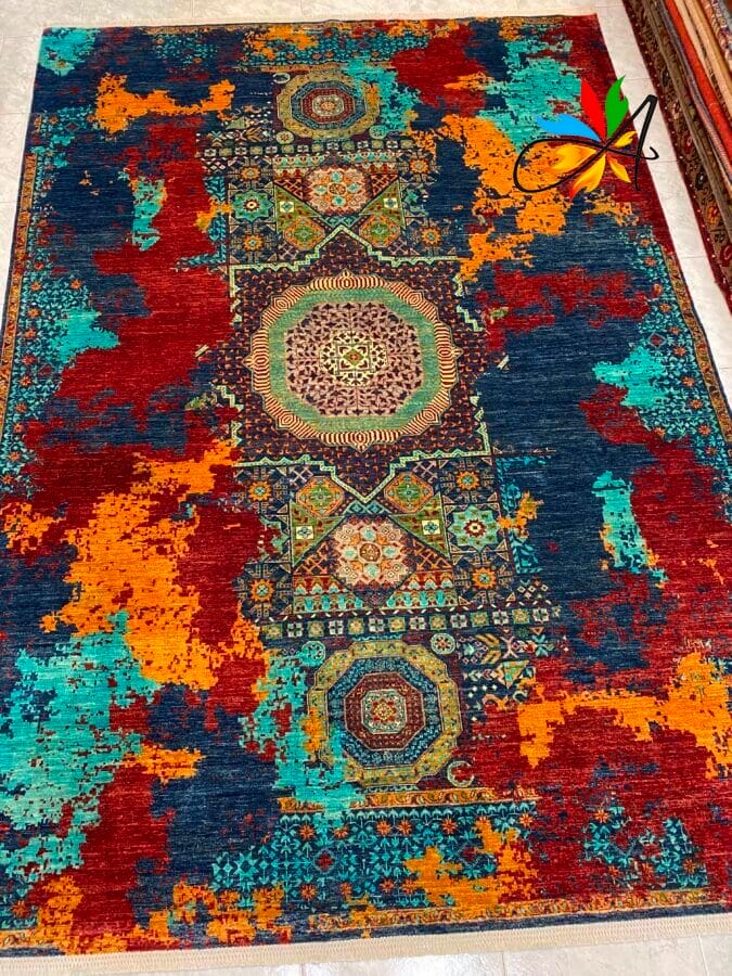 Azerbaijan Tappeti Milano Un tappeto colorato con intricati motivi geometrici e floreali, caratterizzato da audaci tocchi di rosso, arancione, verde acqua e blu scuro.