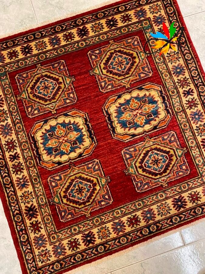 Azerbaijan Tappeti Milano Un tappeto rosso rettangolare con elaborati motivi geometrici e floreali nei toni del blu, dell'oro e del crema.