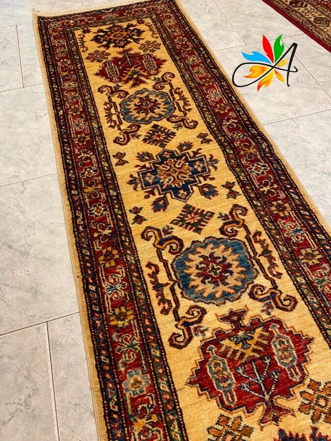 Azerbaijan Tappeti Milano Un tappeto orientale decorato con disegni rossi, blu e marroni su uno sfondo beige, adagiato su un pavimento piastrellato.