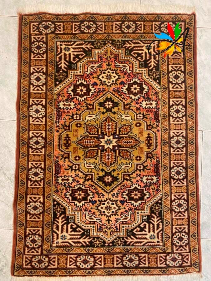 Azerbaijan Tappeti Milano Tappeto decorato con motivi geometrici e floreali in rosso, oro, nero e beige su pavimento piastrellato.