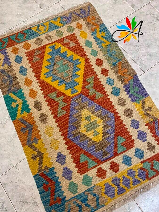 Azerbaijan Tappeti Milano Colorato tappeto intrecciato con motivi geometrici e due grandi rombi, posizionato su un pavimento piastrellato chiaro.