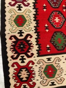Azerbaijan Tappeti Milano Un primo piano di un tappeto tradizionale con intricati disegni geometrici e un motivo centrale nei colori rosso, nero, bianco e verde.