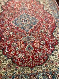 Azerbaijan Tappeti Milano Una vista ravvicinata di un tappeto persiano intricato e colorato con motivi e disegni dettagliati, con la grafica di una farfalla aggiunta nell'angolo superiore.