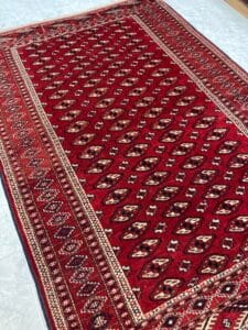 Azerbaijan Tappeti Milano Un grande tappeto tradizionale rosso con intricati motivi geometrici e disegni di bordi disposti su un pavimento.