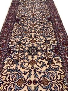 Azerbaijan Tappeti Milano Tappeto a fantasia tradizionale con intricati motivi floreali e di vite in rosso, blu e marrone su uno sfondo crema, delimitato da un dettagliato disegno maroon. Un logo colorato con foglie sovrapposte si trova nell'angolo in alto a destra.