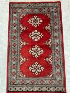 Azerbaijan Tappeti Milano Un tradizionale tappeto rosso con intricati motivi geometrici e dettagli sui bordi, accompagnato da una grafica a farfalla colorata nell'angolo in alto a destra.