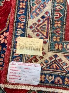 Azerbaijan Tappeti Milano Etichette di autenticità su un tappeto kazak afgano realizzato a mano, che evidenziano i dettagli di origine, qualità e prezzo.