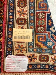 Azerbaijan Tappeti Milano Primo piano di un tappeto kazak orientale tessuto a mano con un'etichetta che indica il tipo, la dimensione e l'origine.