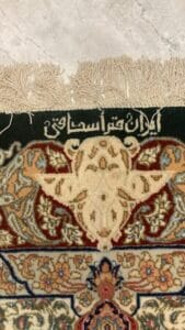 Azerbaijan Tappeti Milano Primo piano di un tappeto ornato con disegni intricati e calligrafia araba, caratterizzato da un motivo multicolore e bordi sfrangiati.