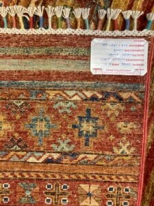 Azerbaijan Tappeti Milano Primo piano di un tappeto a motivi tradizionali con un'etichetta che indica l'origine o l'autenticità.