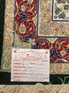 Azerbaijan Tappeti Milano Primo piano di un'etichetta su un autentico tappeto orientale che mostra dettagli come origine, qualità, composizione, dimensione e prezzo, con una sezione del motivo del tappeto sullo sfondo.