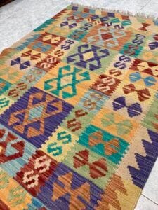 Azerbaijan Tappeti Milano Tappeto colorato tessuto a mano con motivi geometrici visualizzati su un pavimento piastrellato.