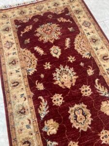 Azerbaijan Tappeti Milano Un lussuoso tappeto a motivi tradizionali con disegni floreali rosso intenso e beige, disposto su un pavimento.