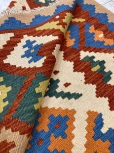 Azerbaijan Tappeti Milano Un primo piano di un tappeto colorato con motivi geometrici, parzialmente ripiegato per mostrare sia la parte superiore che quella inferiore.