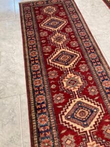 Azerbaijan Tappeti Milano Un tappeto a motivi rossi e blu steso su un pavimento piastrellato.