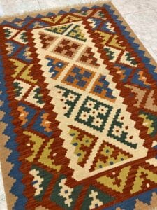 Azerbaijan Tappeti Milano Tappeto tessuto a mano esposto su una superficie piana con motivi intricati e un motivo a farfalla colorato in un angolo.