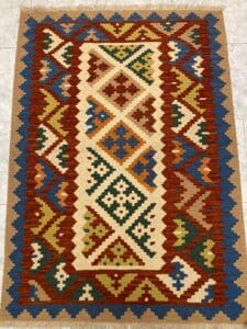 Azerbaijan Tappeti Milano Un tappeto colorato con motivi geometrici disposto su un pavimento piastrellato e una farfalla giocattolo a carica posizionata nell'angolo in alto a destra.