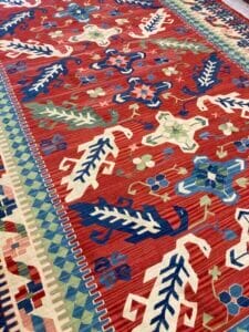 Azerbaijan Tappeti Milano Un vivace tappeto kilim, decorato con tonalità rosse, blu e verdi, giace con grazia sul pavimento.