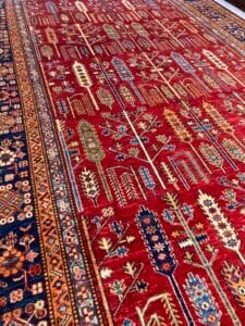 Azerbaijan Tappeti Milano Una vista dettagliata di un tappeto tradizionale riccamente decorato con disegni intricati e una tavolozza colorata, caratterizzato da un piccolo logo o oggetto in basso al centro che aggiunge un tocco di modernità all'arte tessile senza tempo.