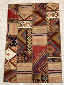 Azerbaijan Tappeti Milano Un tappeto patchwork colorato esposto sul pavimento con una vivace decorazione a farfalla posizionata nell'angolo in alto a destra.