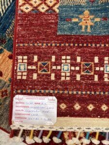 Azerbaijan Tappeti Milano Una fotografia in primo piano di un tappeto fatto a mano con un'etichetta informativa sul prodotto attaccata, che mostra dettagli come origine, dimensioni, qualità e prezzo.