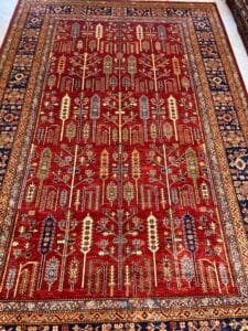 Azerbaijan Tappeti Milano Un intricato tappeto persiano con rossi ricchi e motivi geometrici complessi, ornato da una farfalla colorata che ne abbellisce la trama rigogliosa.