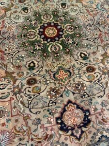 Azerbaijan Tappeti Milano Un tappeto persiano tradizionale e ornato presenta un intricato motivo floreale e geometrico in colori ricchi, tra cui verde, rosso, blu e beige. Un logo colorato con foglie e una linea nera appare nell'angolo in alto a destra.