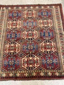 Azerbaijan Tappeti Milano Tappeto orientale colorato a motivi geometrici con forme rosse, blu, bianche e verdi su un pavimento piastrellato.