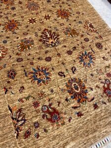 Azerbaijan Tappeti Milano Tappeto a fantasia marrone con disegni floreali colorati e un logo a forma di foglia multicolore nell'angolo in alto a destra.